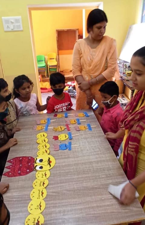 Children and teachers around a table with a paper caterpillar made of smiley faces