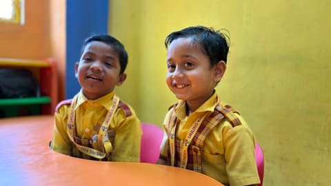 Two smiling children in school uniform at a classroom table