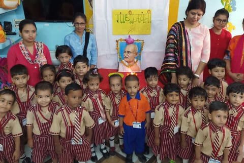 Children in school uniform with their teachers in front of a garlanded portrait of Mahatma Gandhi on Gandhi Jayanti
