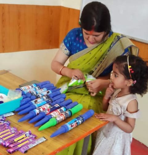 A teacher and a little girl with pichkaris and colours laid out on a table