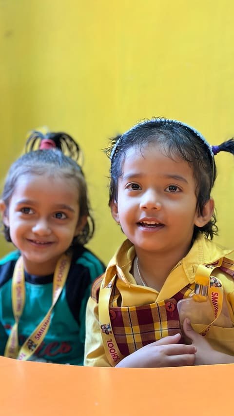 Two young children smiling at a classroom table