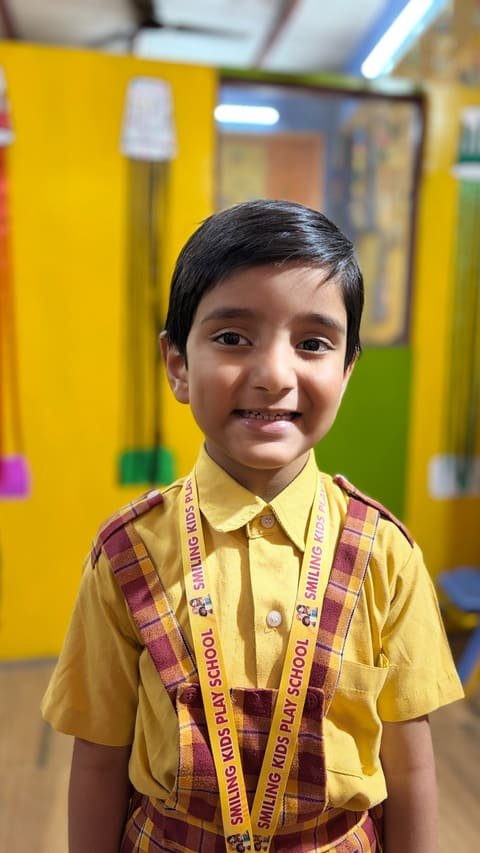 A smiling boy wearing the school uniform and Smiling Kids Play School lanyard