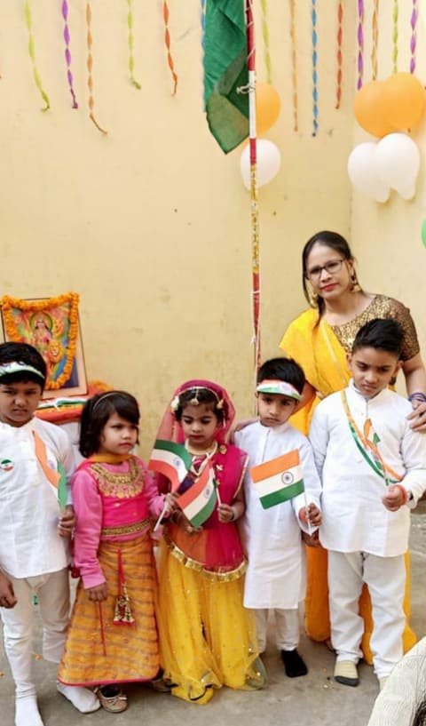 Children in traditional clothes holding Indian flags with their teacher under tricolour balloons