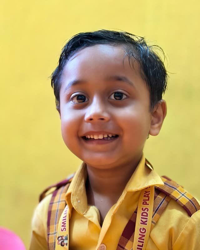 A cheerful boy in school uniform in a yellow-walled classroom