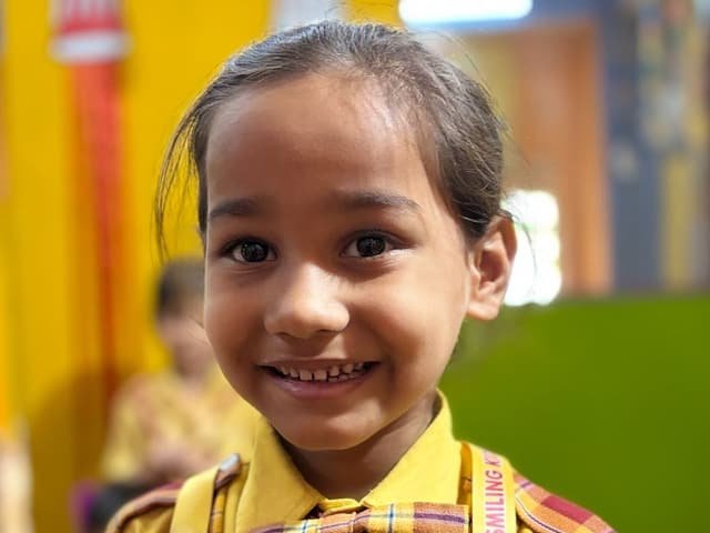 A smiling girl in the yellow and maroon school uniform inside a classroom