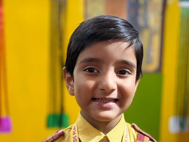 A smiling boy wearing the school uniform and Smiling Kids Play School lanyard